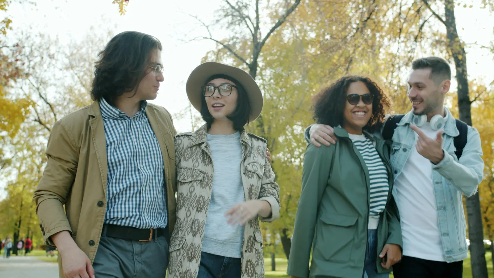 Quatre personnes marchent et discutent avec le sourire dans un parc en automne